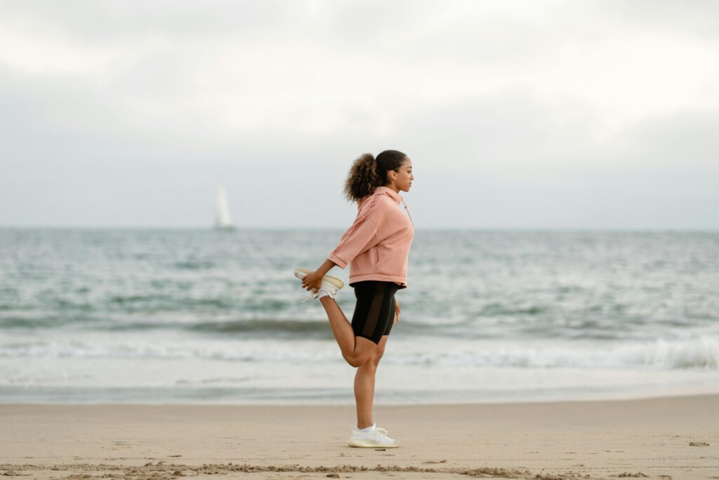 pexels-photo-4909526-4909526 Side view of a woman in activewear stretching while performing yoga on a beach.